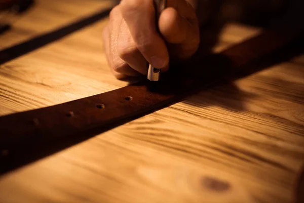 Proceso de trabajo del cinturón de cuero en el taller de cuero. Hombre sosteniendo herramienta de elaboración y trabajo. Tanner en curtiduría vieja. Fondo de tabla de madera. Cerca del brazo del hombre —  Fotos de Stock