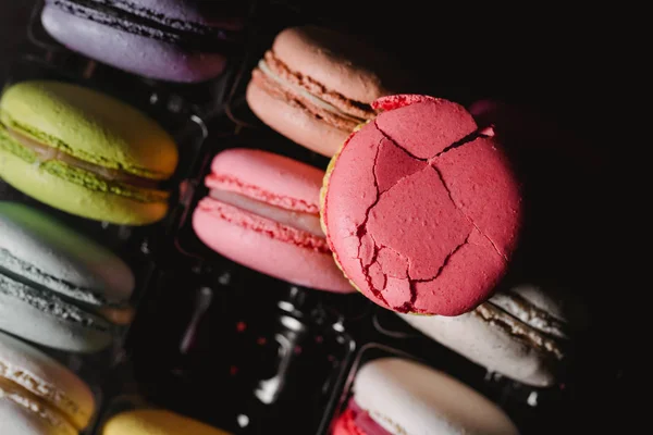 Empty place in box. Colorful rumpled macaroon on top. Closeup food photo with black background