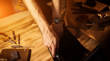 Deri kemer deri atölyesinde çalışma süreci. Adam holding aracı. Tanner eski Tabakhane içinde. Ahşap masa arka plan. Adam kolunu kapatın. Sıcak ışık metin ve tasarım için. Web afiş boyutu