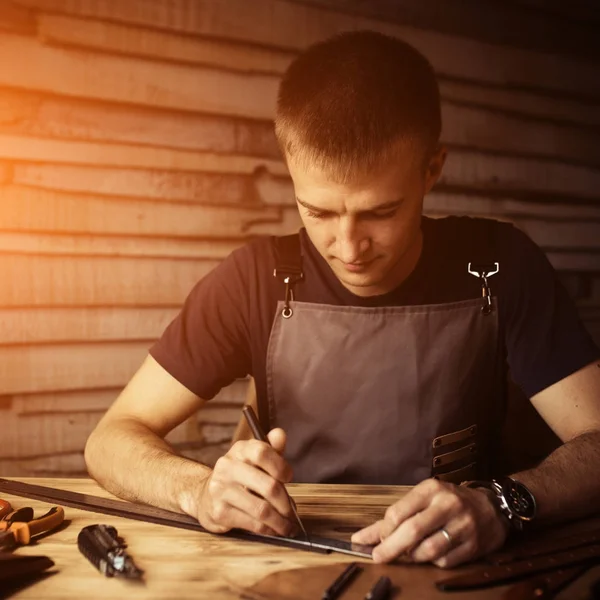 Arbeitsprozess des Ledergürtels in der Lederwerkstatt. Mann hält Werkzeug in der Hand und arbeitet. Gerber in der alten Gerberei. Holztischhintergrund. warmes Licht für Text und Design — Stockfoto