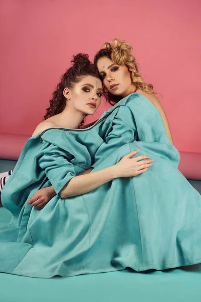 Close up indoor studio fashion portrait of gorgeous women in stylish blue clothes. Blonde and brunette girls on mint-pink background. Full-length shot of glad curly models — Stock Photo, Image