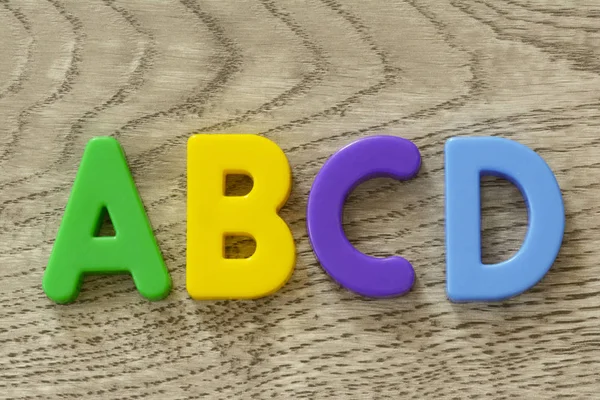 Κεφαλαία γράμματα A B C D σε επίπεδη πολύχρωμο πλαστικό γράμμα παιχνίδια στην ανάγλυφη επιφάνεια γκρι ξύλινο — Φωτογραφία Αρχείου