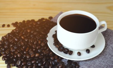 Beyaz fincanda siyah espresso ve ahşap masada kahve çekirdeği.