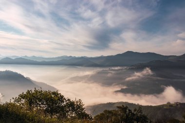 Gün ışığında sisle kaplı bir vadinin manzarası. Bir vadinin üstünden, yüksek dağlardan ve kısmen bulutlu bir gökyüzünden bak. İspanya 'nın kuzeyinde (Asturias) yer alan seyahat modu
