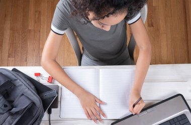 Beyaz ofis masasında dizüstü bilgisayar kullanarak ev ödevi okuyan bir kadın, karantina ve kendini izole etme süresince.