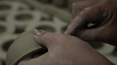 Atölye. Kadınların elleri kilden kupayı okşar, kusurlarını temizler. Gri tonlu. Kapat..