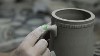 Atölye. Yeşil tırnaklı kadın elleri, kulpu kil kupaya yapıştırıyor. Gri tonlu. Kapat..