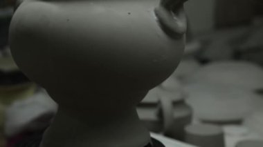 Clay atölyesi. Boyanmamış bir kil semaveri tezgahına döner. Açık panorama. Gri tonlarda.
