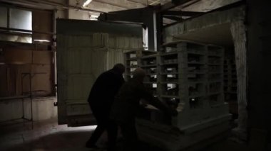 Mutfak malzemeleri dükkânı. İki adam taşınabilir bir toprak takımını fırına itiyor. Soldan sağa. Büyük plan. Gri Tonlama.