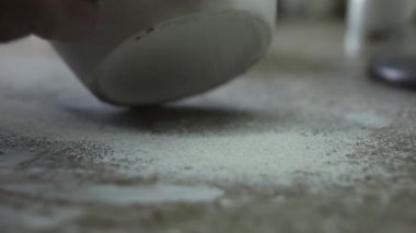 Kazıyıcı sürahinin yüzeyini öğütüyor. Masaya bir kil kırıntısı düşüyor. Kapatın. Gri Tonlama.