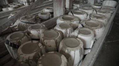 Atölye. Toprak kapları ahşap raflarda duruyor. Yavaş panorama ileri. Gri tonlu. Bakış açısı. Genel plan.