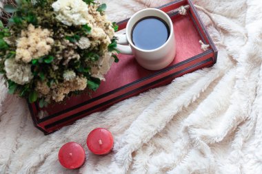 Bir fincan kahve ya da çay, kuru çiçekler ve beyaz, kırmızı mumlar, bej bir battaniyede kırmızı ahşap bir kutu