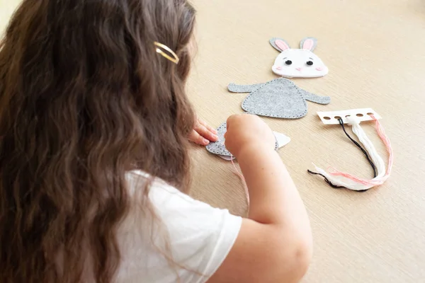 child girl sews a toy made of felt sitting at the table