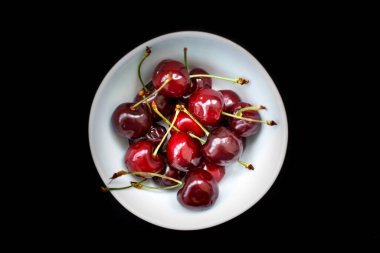 Siyah arka planda beyaz bir kasede kırmızı kirazlar, izole.