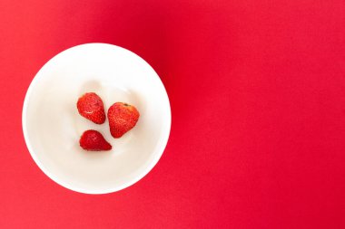 Kırmızı arka planda beyaz bir tabakta üç kırmızı çilek, izole edilmiş.