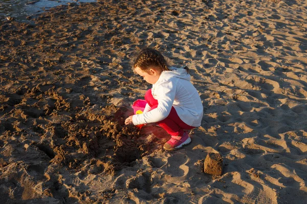 a girl plays with sand on a sandy beach on the river Bank during sunset
