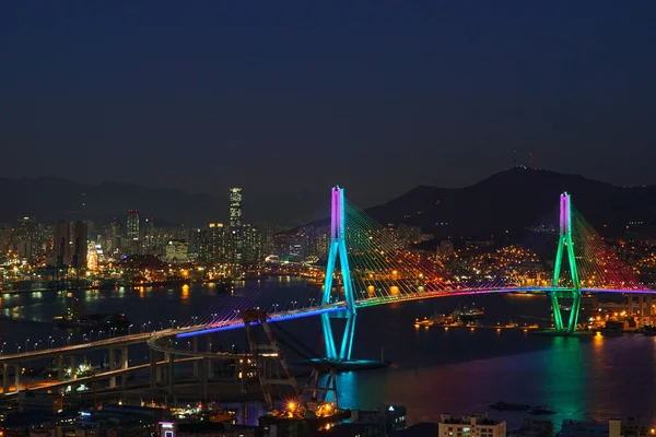 Yeşil ve mavi ışıklarla parlayan bir köprü. Busan Köprüsü.