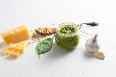 Cam kavanozda yeşil pesto fesleğen sosu yakın plan. Beyaz arkaplan boşluğunda parmesan fesleğen ve çam fıstığı içerir..