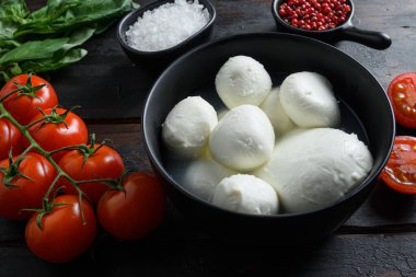 Mozzarella peynirli toplar, kiraz domatesleri ve yeşil taze organik fesleğen biberleri ahşap masa seçici odak noktasında..