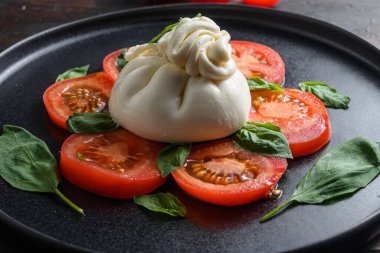 El yapımı burrata peyniri taze domates ve fesleğen yapraklarıyla servis edilir. Geleneksel İtalyan salatası.