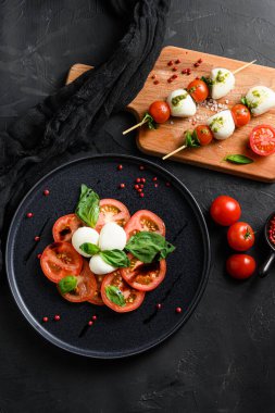 Caprese salatası domates ve fesleğen yapraklı mozzarella dilimleri şiş üzerinde ve siyah seramik platwantipasta siyah desenli arka plan görüntüsü