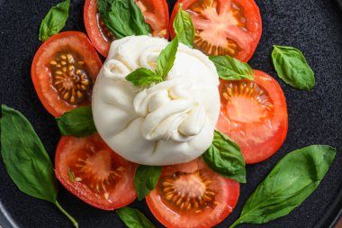 Taze domates ve fesleğen ile servis edilen el yapımı burrata peyniri. Geleneksel İtalyan salatası.