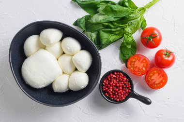 İtalyan Caprese salatasının içeriği olan taze fesleğen yapraklı ve kiraz domatesli Mozzarella peyniri topları beyaz arka planda..