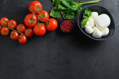 Mozzarella peynirli topları, kiraz domatesleri ve yeşil taze organik fesleğenli İtalyan mutfağı. Caprese Organik Akdeniz gıda konsepti için malzemeler, metin için düz bir üst görünüm alanı. Siyah masa.