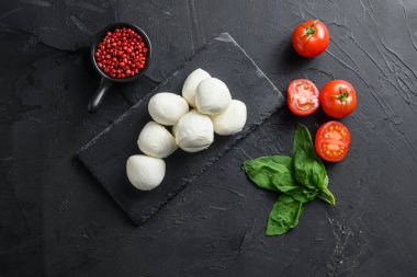 Mozzarella peyniri, fesleğen domates vişnesi eski siyah arka plan üzerinde siyah taş yazı tahtası uzayı.