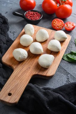 İtalyan Caprese salatasının içeriği olan taze fesleğen yapraklı ve kiraz domatesli bufalo Mozzarella peynir topları siyah bir bez ve gri beton arka planda dikey yakın plan.