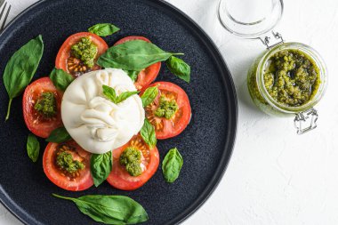Burrata Buffalo peyniri taze domates ve fesleğen yapraklı pesto sosuyla servis edilir. Siyah tabakta beyaz arka planda. .