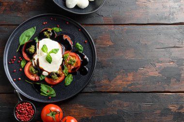 İtalyan yemeği - dilimlenmiş domatesli caprese salatası, mozzarella peyniri, fesleğen, zeytinyağı. Koyu ahşap arka planda siyah tabakta servis edilmiş. Üst Manzara. Kırsal tarzda. Metin yatay için boşluk.