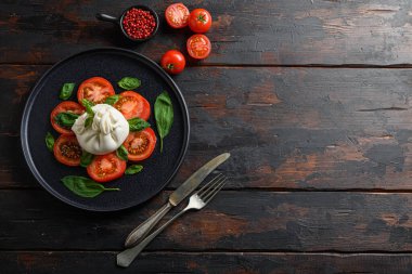 Burrata, krema ve inek sütünden yapılmış İtalyan taze peyniri. Siyah tabakta eski ahşap masa tahtalarında eski bıçak ve çatal için üst görüş alanı.