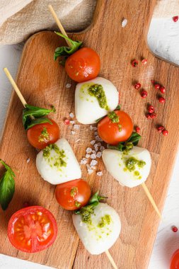 Çubuklarda Caprese salatası, Cherry domatesleri, mozzarella peyniri, fesleğen, ahşap tahtada pesto sosu, beyaz kırsal arka plan manzarası..
