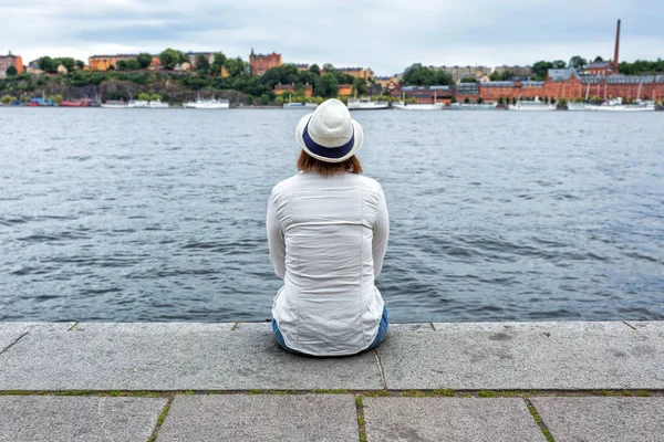 Femme avec chapeau assis sur le rocher près de la mer — Photo