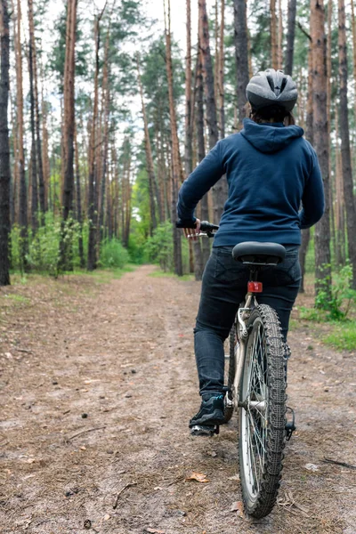 Girl on bicycle rides at the road in coniferous forest