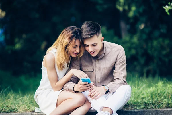 Cople met behulp van een smartphone, zittend in het park — Stockfoto