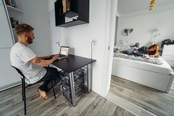 Papa arbeitet am Laptop, Mama und Baby auf dem Bett — Stockfoto