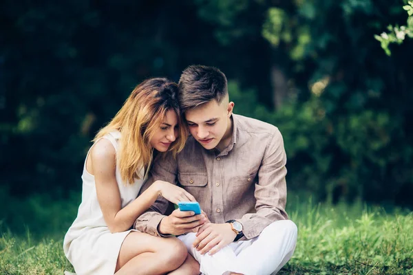 Cople pomocí smartphone, sedí v parku — Stock fotografie