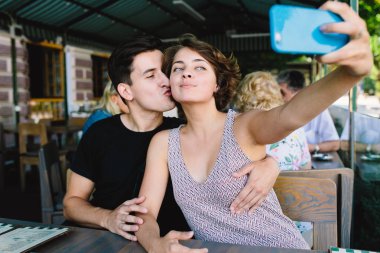 Erkek ve kız dışarıdaki kafede selfie çekiyorlar.