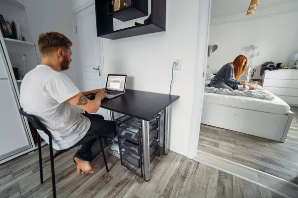 Papà lavora al computer portatile, mamma e bambino sul letto — Foto Stock