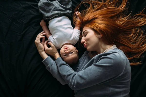 Happy mother with baby lying together on bed — Stock Photo, Image