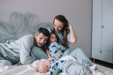 Anne, baba, kız ve bebek yatakta.