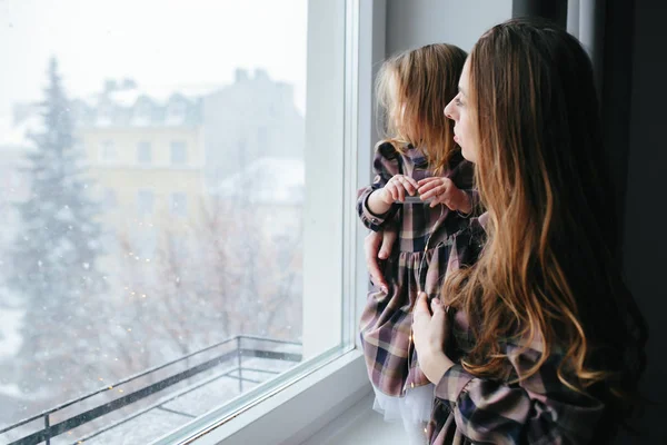 Mom with little girl looking through the window — Stock Photo, Image