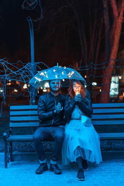Chico y chica sentados en un banco bajo un paraguas — Foto de Stock
