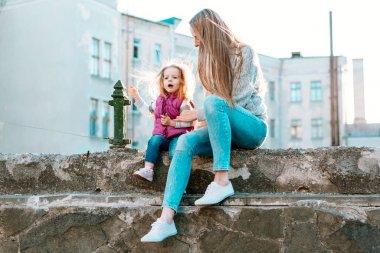 Anne ve kızı çitte birlikte oturuyorlar.