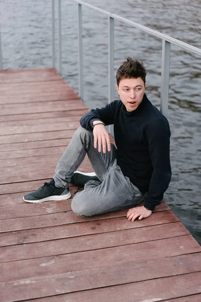 Joven sentado en un muelle de madera — Foto de Stock