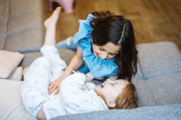 Two sisters playing together on the big couch — Stock Photo, Image