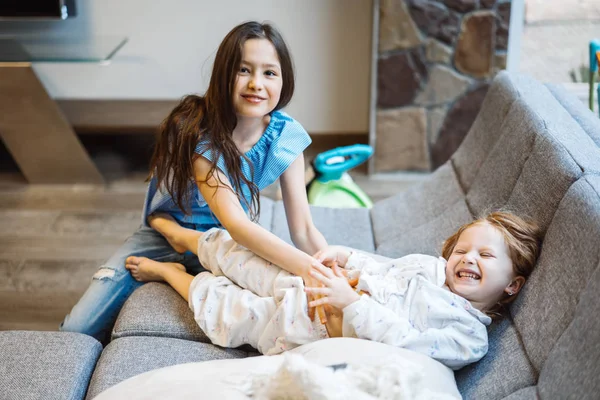 Büyük kanepede birlikte oynayan iki kız kardeş — Stok fotoğraf