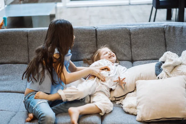 Büyük kanepede birlikte oynayan iki kız kardeş — Stok fotoğraf